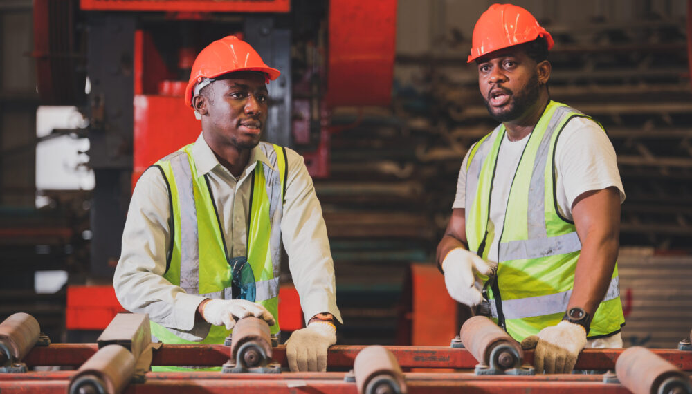 Two people black man African American worker control heavy machine in the factory.