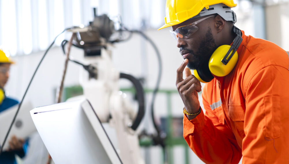 portrait of native american engineer technician wearing safty uniform hand contril automation robot arm welding machine with laptop industrial 4.0 factory background concept