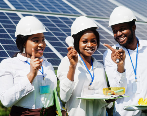 African american technician checks the maintenance of the solar panels. Group of three black engineers meeting at solar station. Hold led bulb.